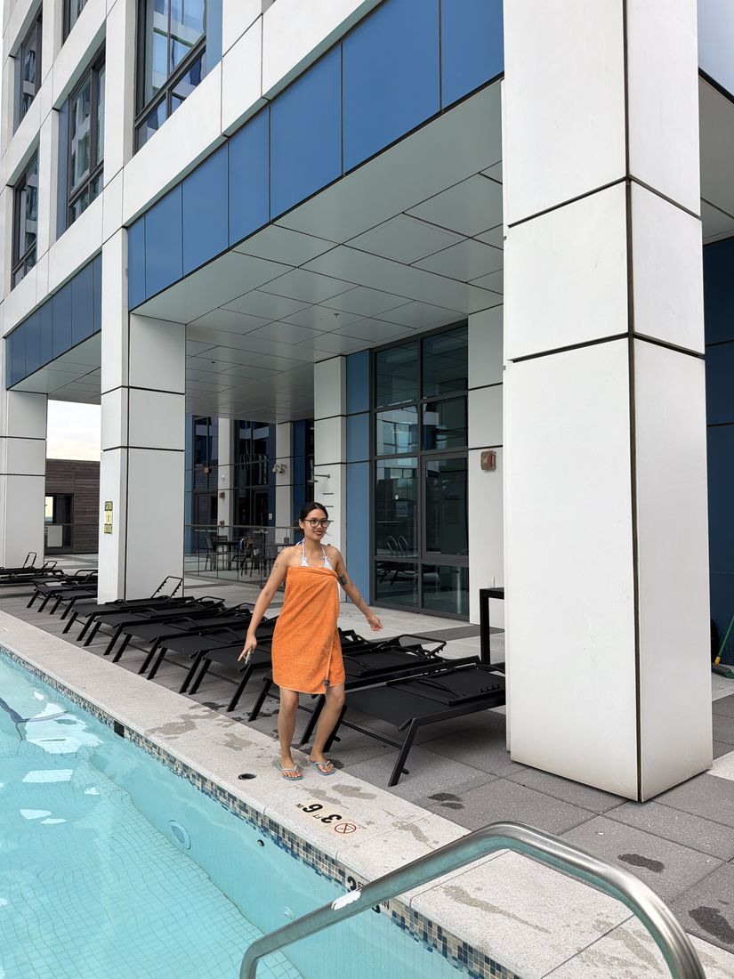 Yas standing by a rooftop pool in an orange towel